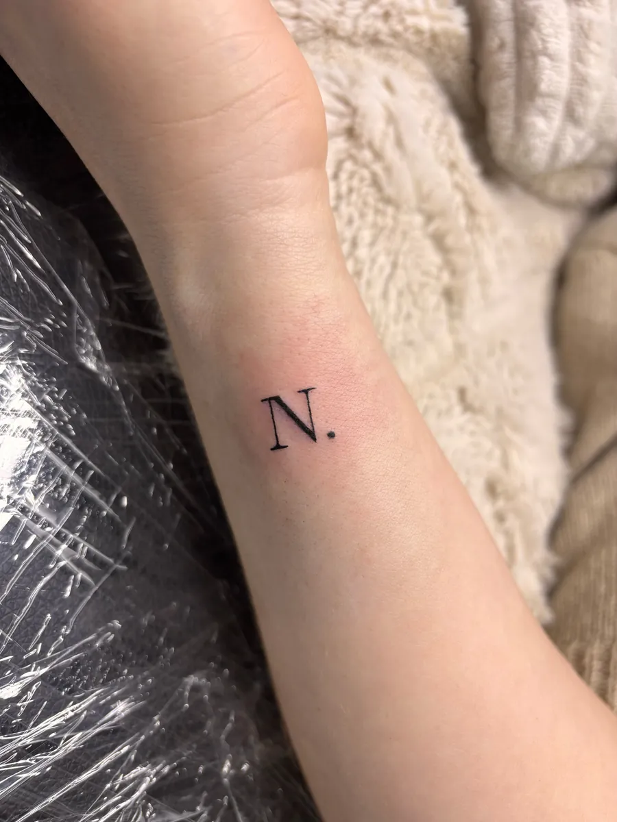 Feiner Buchstabe als kleines Tattoo am Unterarm